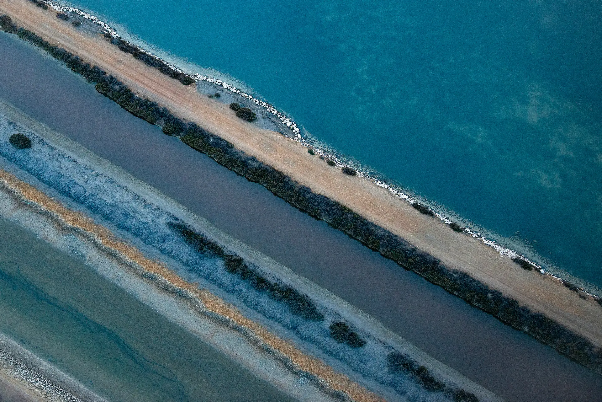 Digue, canal et étang de Camargue en lignes parallèles, vus du ciel